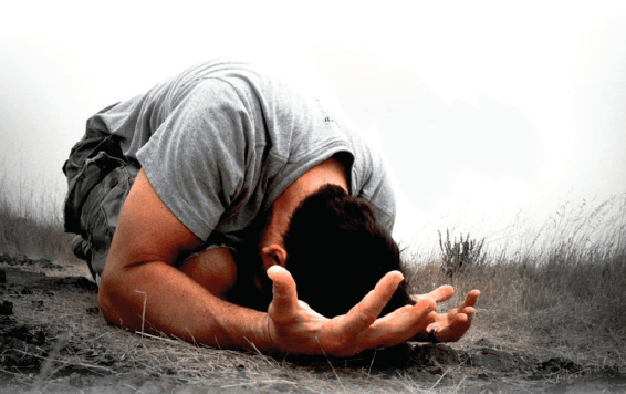 A person in a grey shirt and jeans kneeling on the ground Description automatically generated